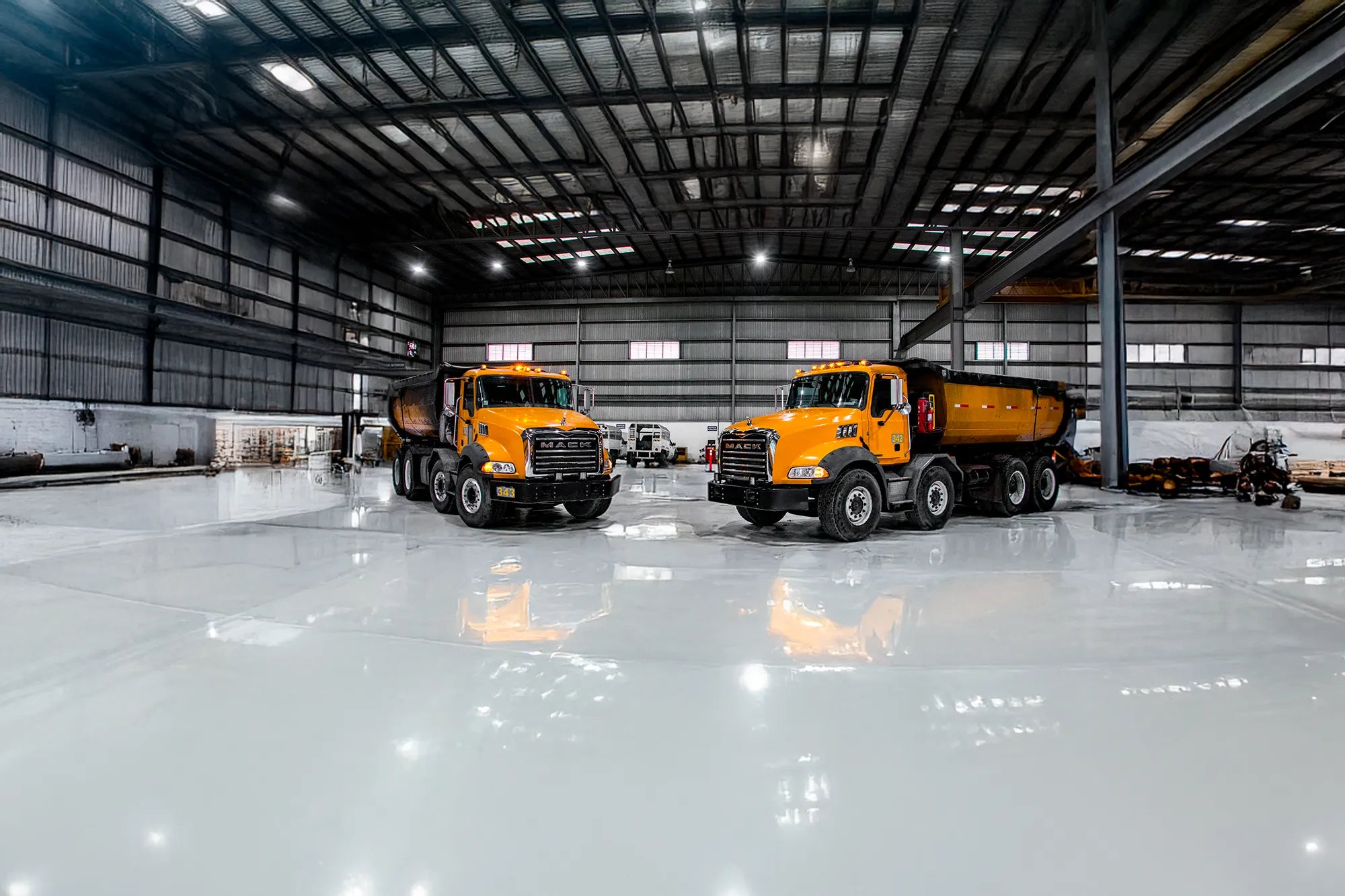 Camiones de volteo Mack Granite seminuevos de color amarillo, en almacén techado.